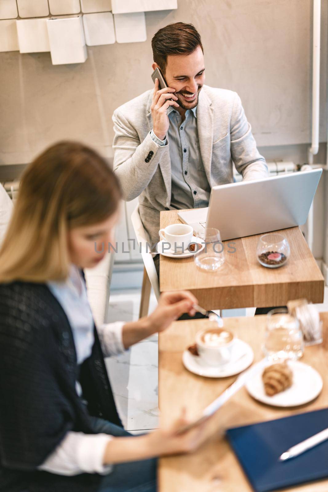 Young businesspeople surfing the internet on a break in a cafe. Smiling man working at laptop and using smarthphone. Young woman using digital tablet and drinking coffee. 