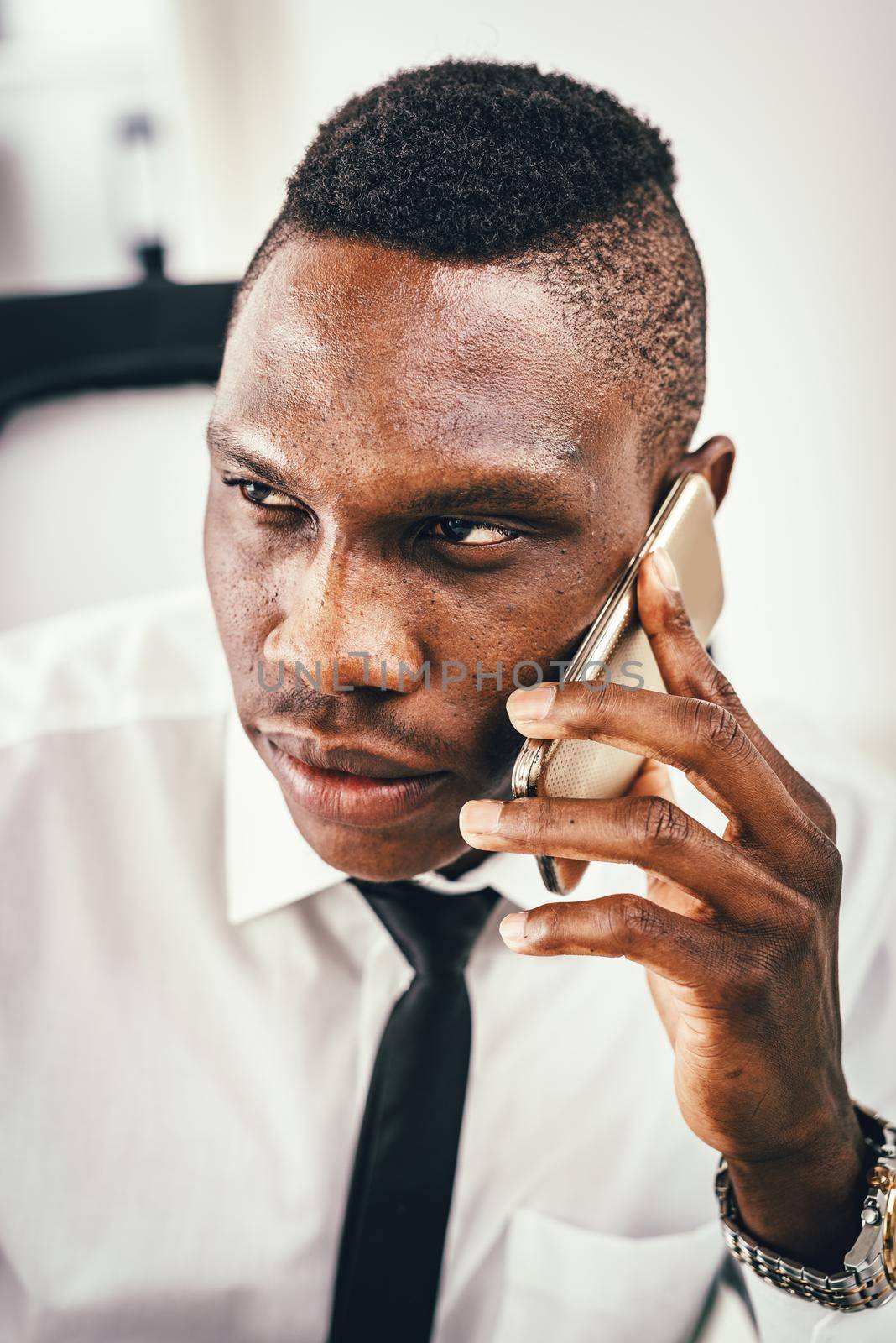 A portrait of a pensive African businessman, who is talking on smartphone in modern office.
