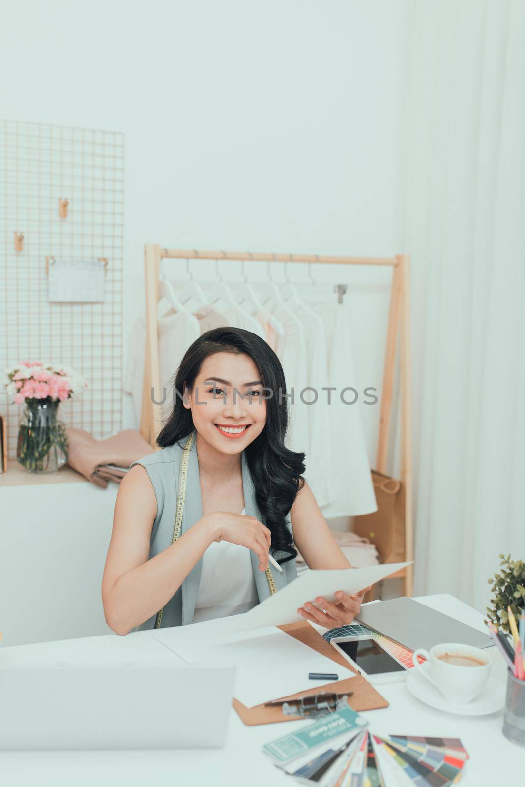 Fashion designer at work. Happy young Asian woman drawing while sitting at her working place in fashion workshop