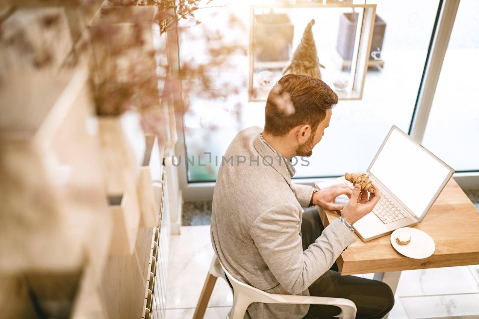Young businessman on a break in a cafe. He is working at laptop and using having breakfast. 