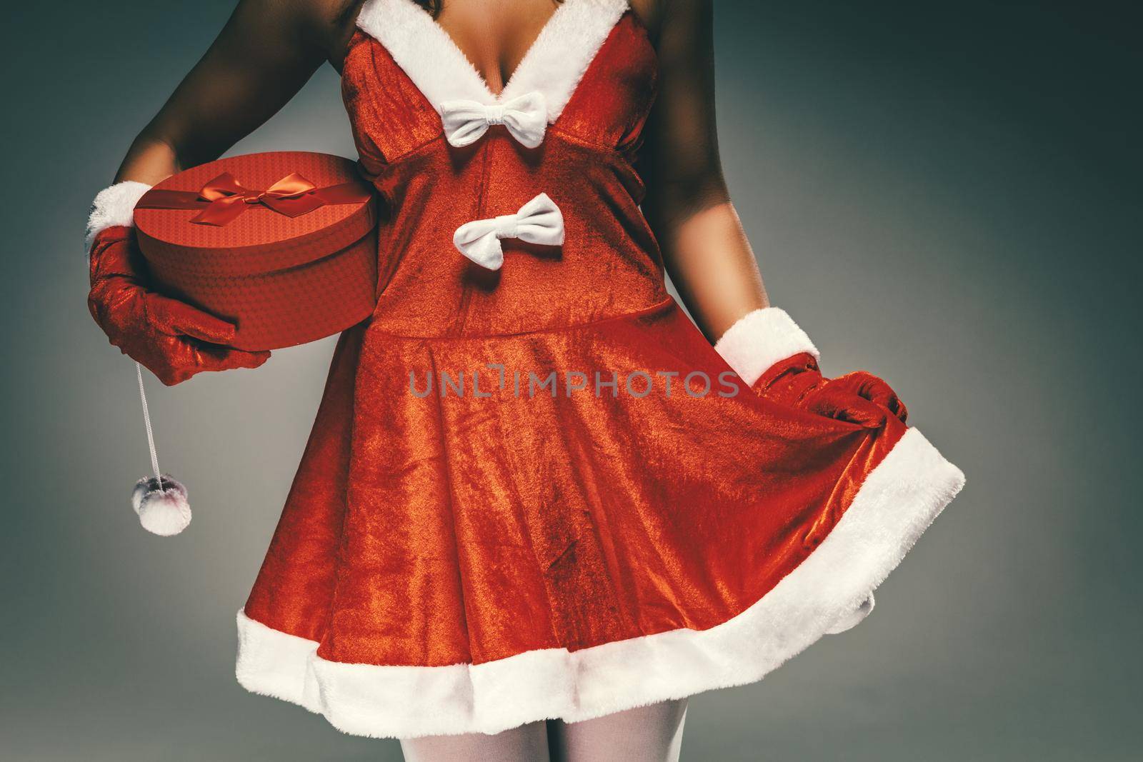 Close-up of a young unrecognizable woman in Santa Claus costume holding red present.