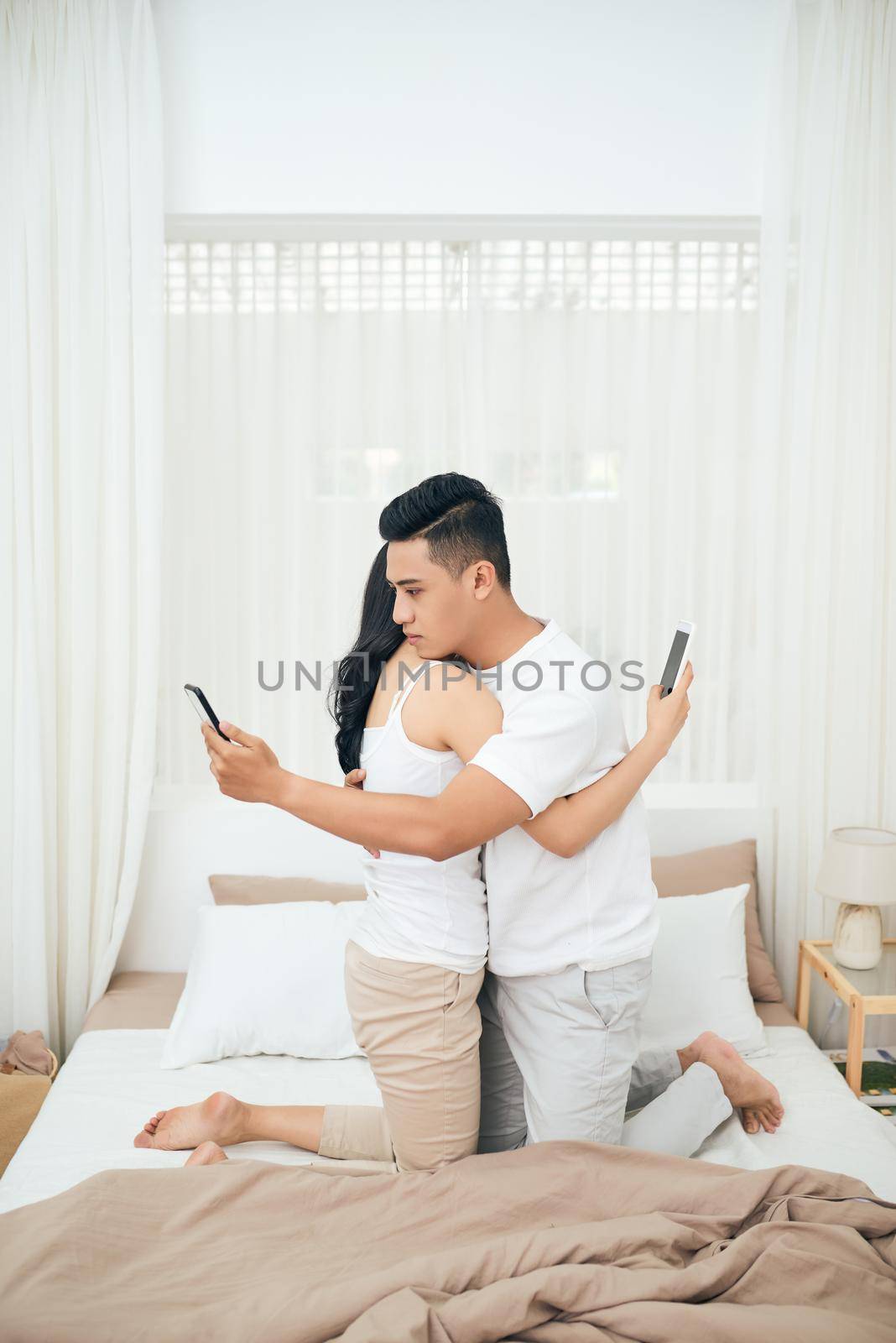 Young couple in the bedroom. Side view of unfaithful man and woman are cheating on the phone while hugging each other