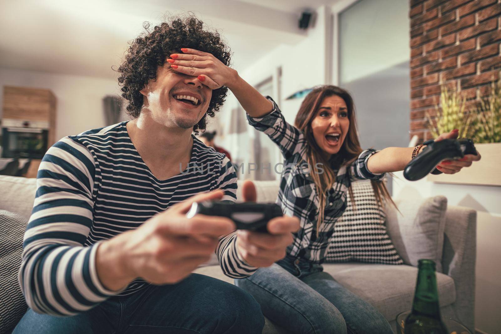 Excited couple is playing video games at home sitting on sofa. They have great weekend in nice company indoors. 