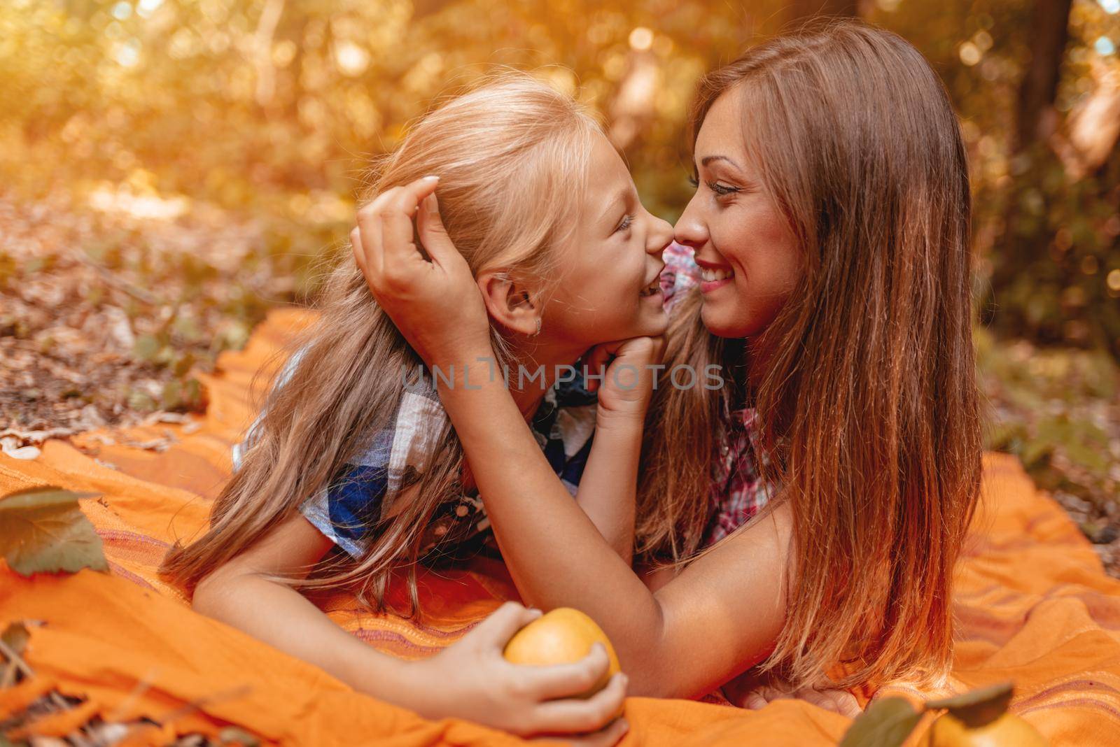 It's the autumn season and beautiful mom and her little girl is lying down in a forest full of autumn leaves and enjoying. 
