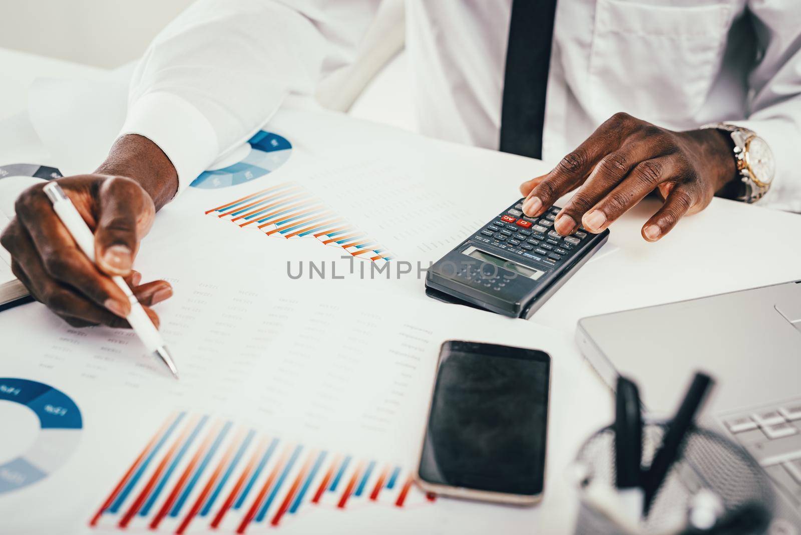 Close-up of a hands of African businessman working on calculator in the modern office.