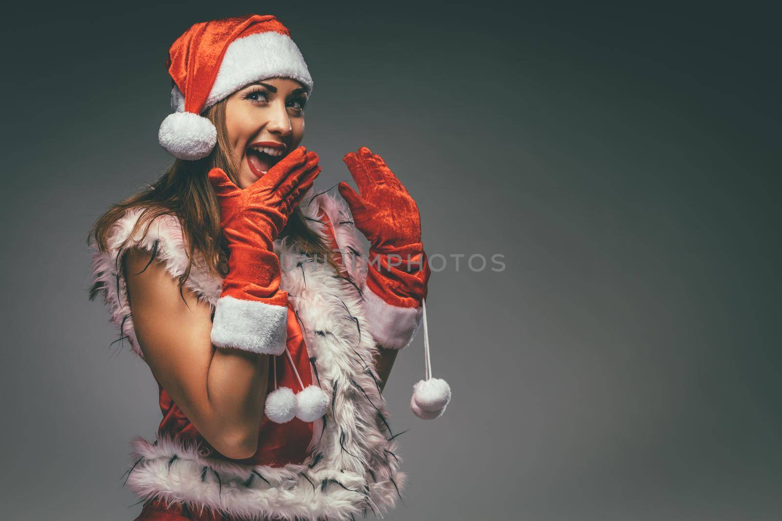 Portrait of a beautiful young smiling woman in Santa Claus costume having fun and surprised looking at camera.