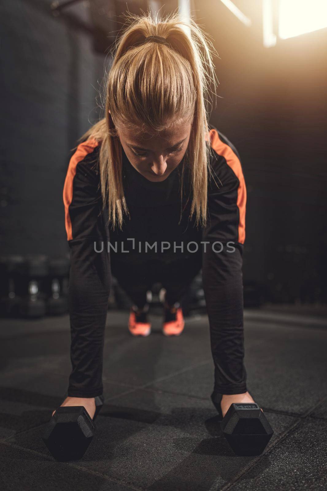 Young muscular  beautiful  woman doing push up exercise with dumbbell on hard workout at the gym.
