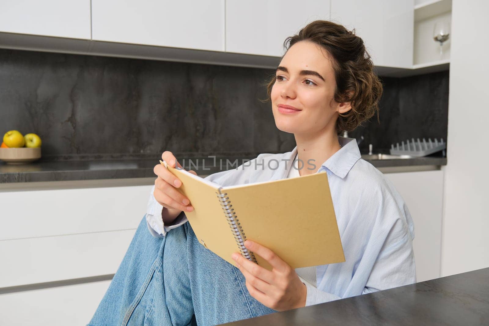 Portrait of young adult woman, reading her notes, holding notebook and smiling, relaxing at home.