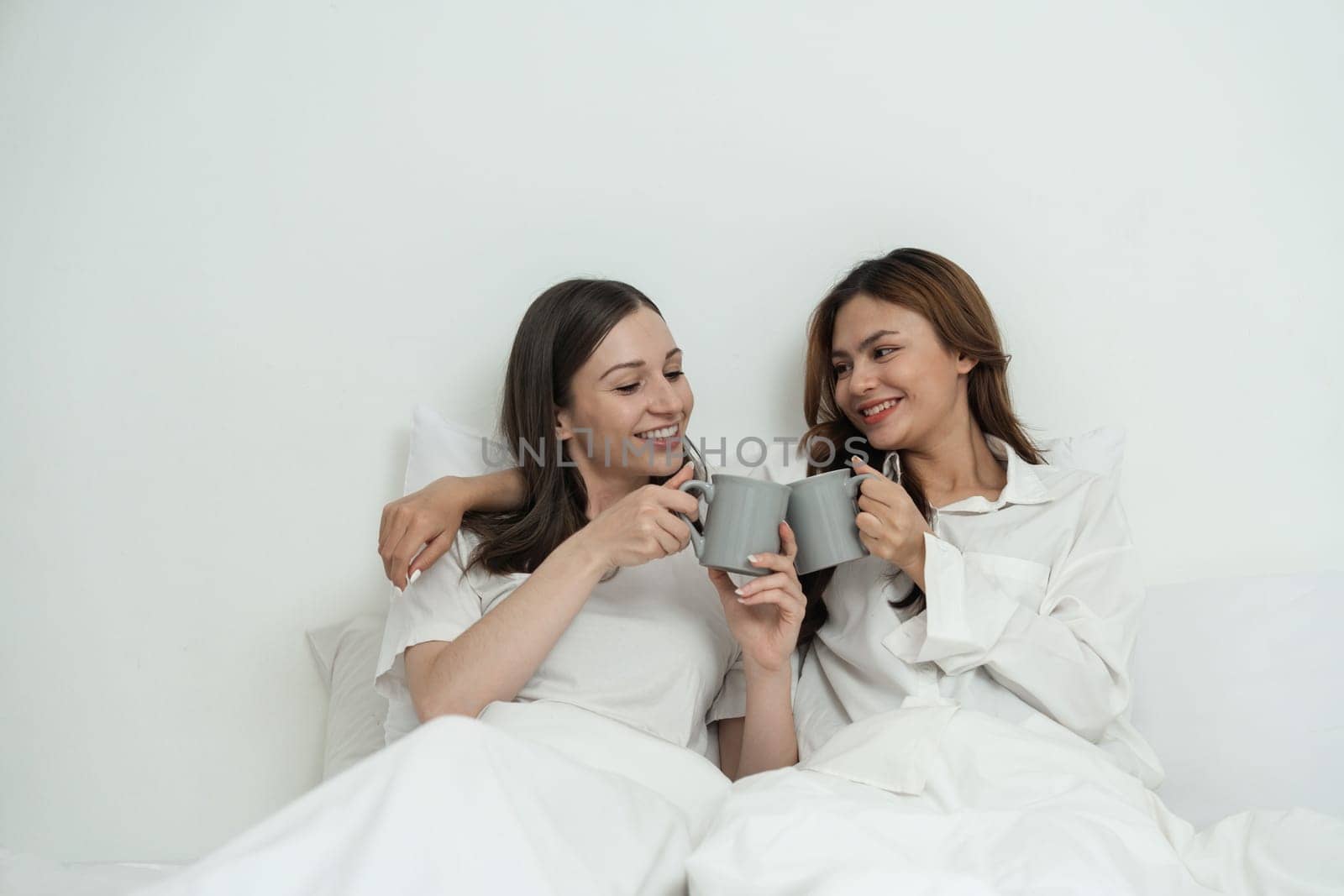 Two Asian cheerful happy female girlfriends having a coffee sitting on the bed. Concept lifestyle lesbian couple.