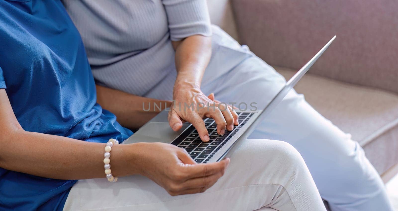 two 60s woman enjoy with social media on her laptop on a sofa by wichayada