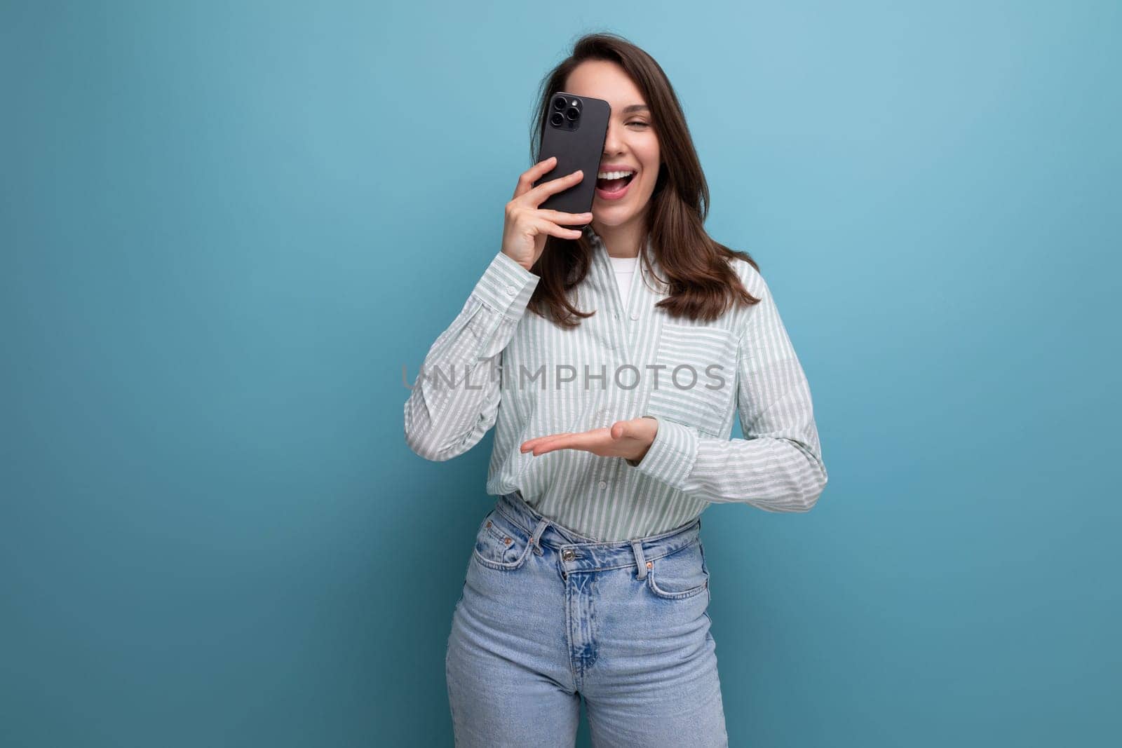 cute young brunette woman in a shirt makes a photo on a smartphone on a studio background.