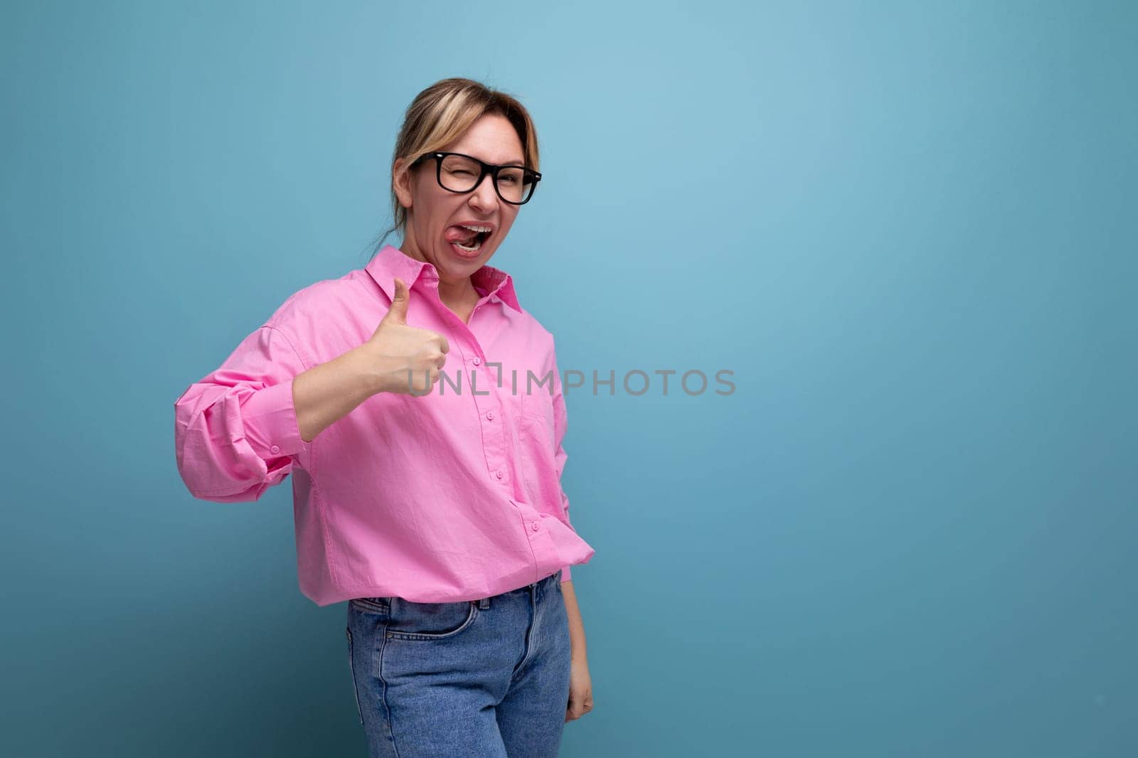confident positive young blond caucasian woman model with ponytail hairstyle in a stylish look consisting of a pink blouse and jeans.