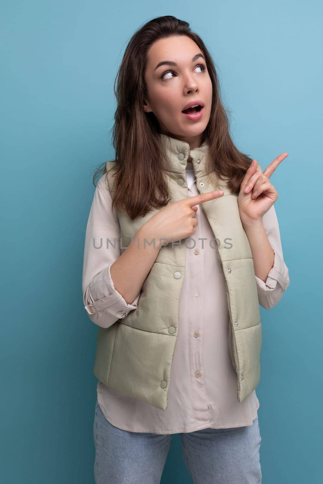 young brunette woman in a shirt and vest points a finger for ideas and inspiration on a background with copy space.