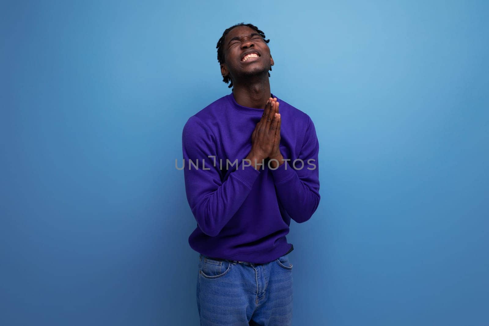 praying black american young brunette man with dreadlocks in a blue hoodie.