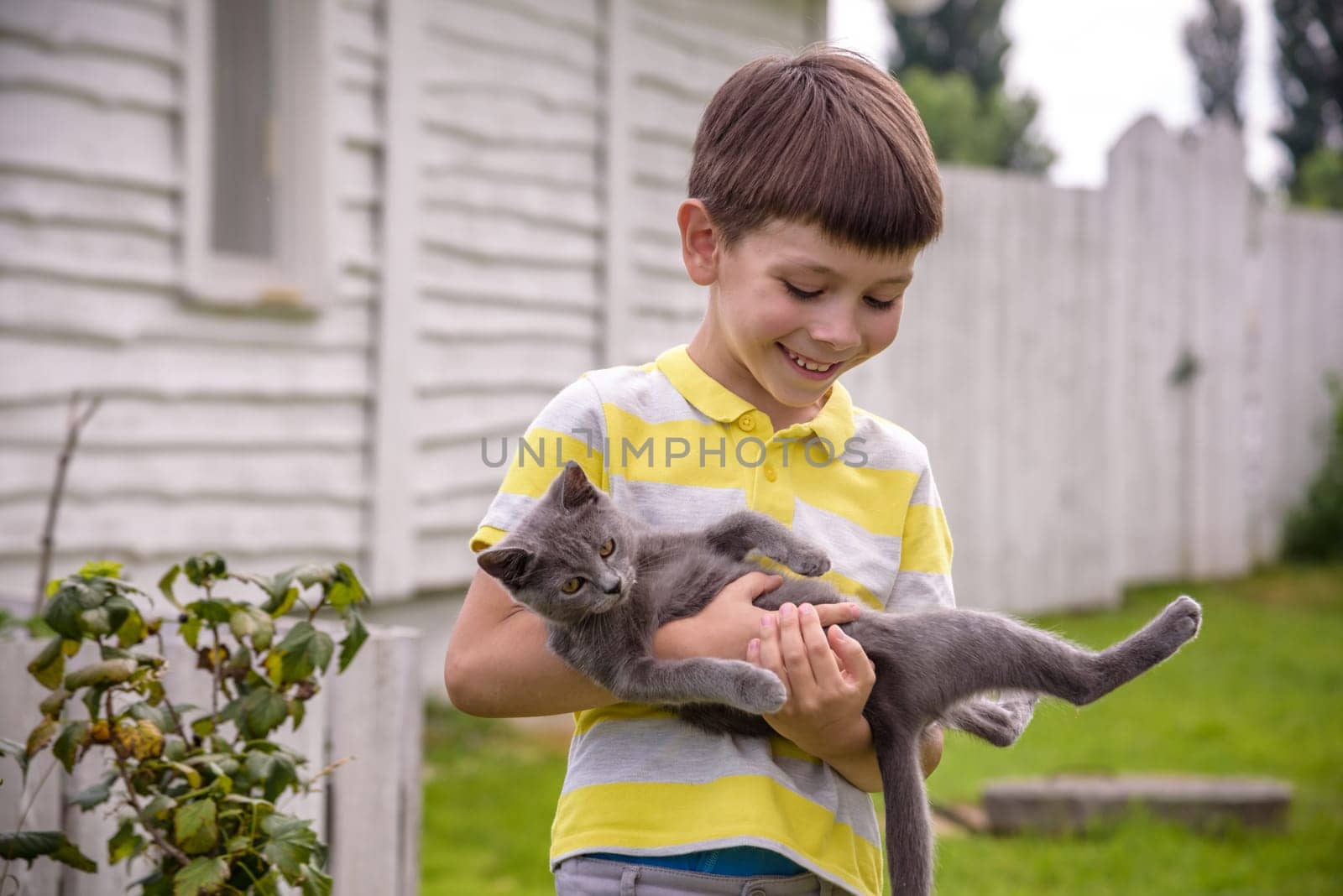 Funny boy hugging a cat with lots of love. Portrait of child holding on hands a Kitten. Playing with a cat on village countryside.