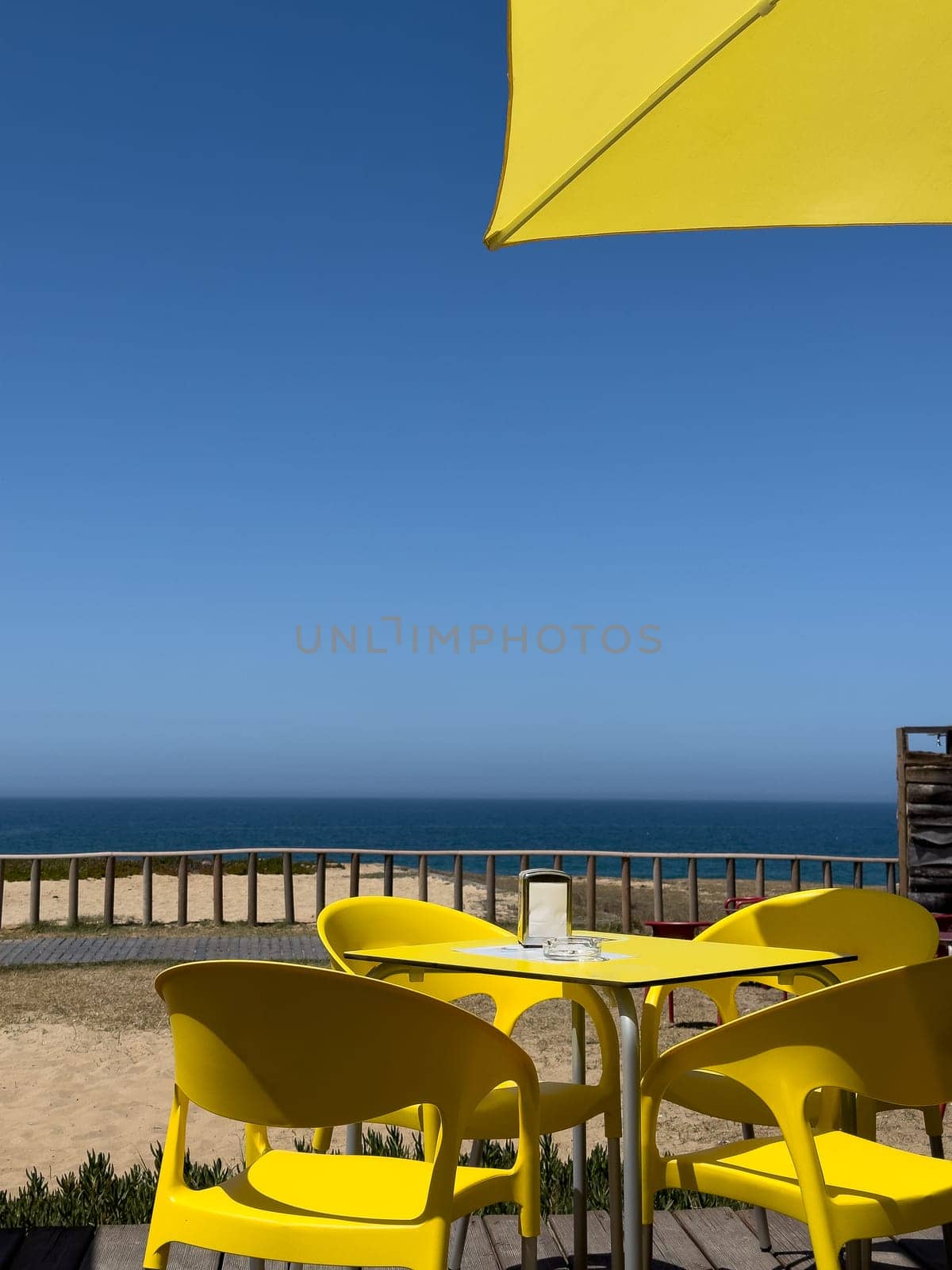 View of the ocean from a table with four chairs and a yellow umbrella.