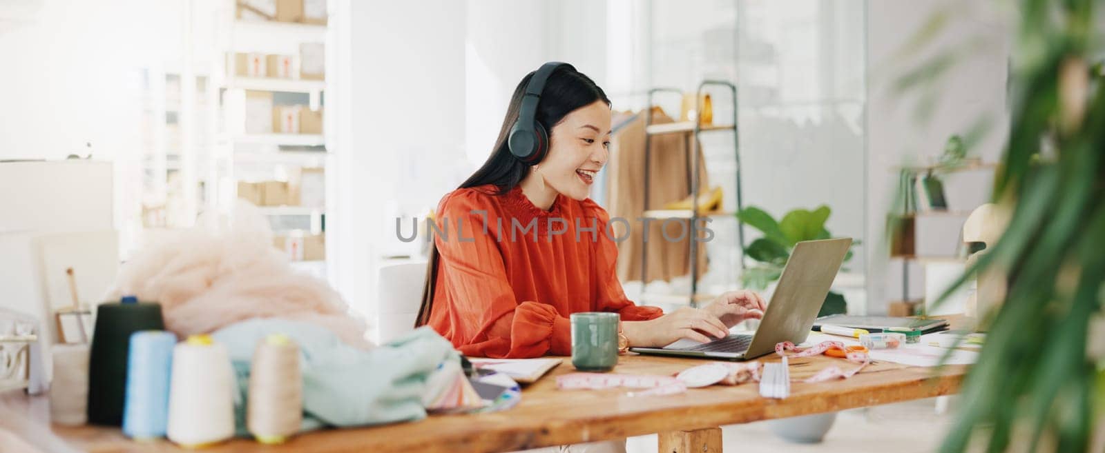 Video call, laptop and ecommerce with asian woman and headphones in warehouse for networking, fashion and design. Online shopping, meeting and conference with girl for clothes, startup and retail.