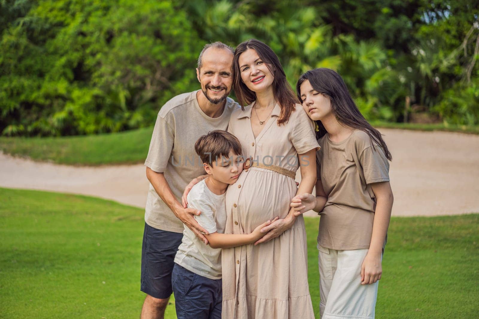 A loving family enjoying a leisurely walk in the park - a radiant pregnant woman after 40, embraced by her husband, and accompanied by their adult teenage children, savoring precious moments together amidst nature's beauty. Pregnancy after 40 concept by galitskaya