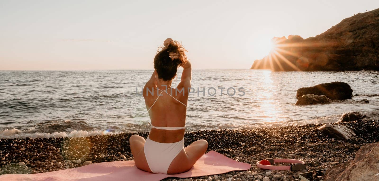 Woman sea yoga. Happy woman in white swimsuit and boho style braclets practicing outdoors on yoga mat by sea on sunset. Women yoga fitness routine. Healthy lifestyle, harmony and meditation by panophotograph