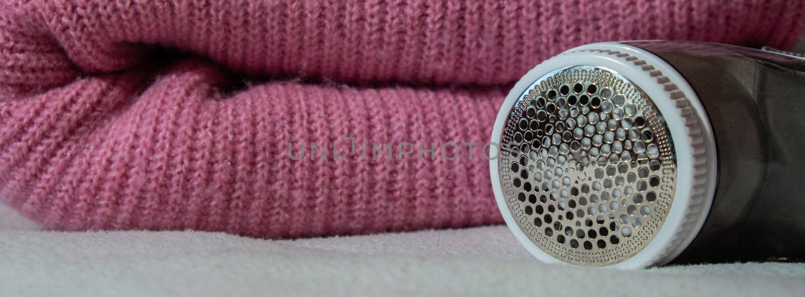 Anti-pilling razor. Device for shaving clothes. Anti-Plush fabric Shaver. Electric portable sweater pill defuzzer Lint remover from pink acrylic or wool sweater. Electric device fabric shaver after cleaning and collected fluff by anna_stasiia