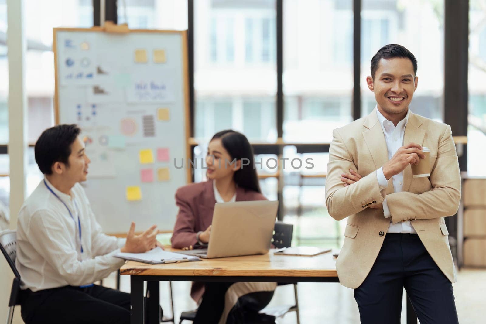 Portrait of happy and confident young man against background of his business team colleagues.