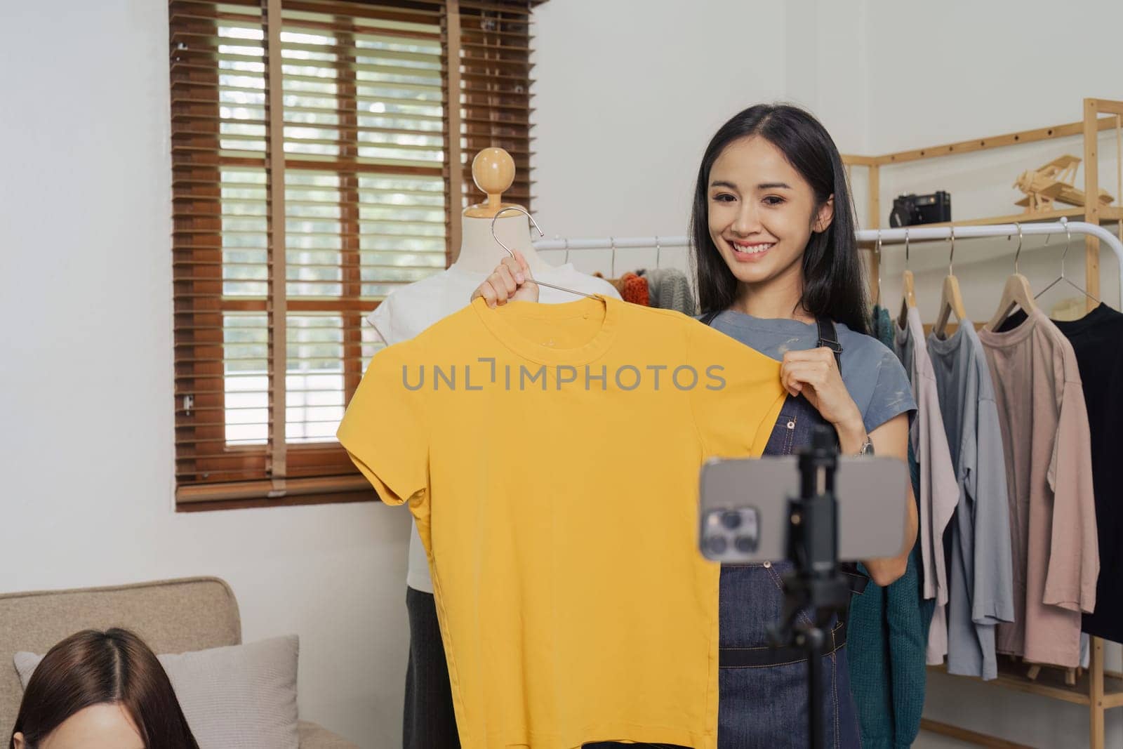 Beautiful asian woman showing clothes for sale in front of camera for live streaming at home.