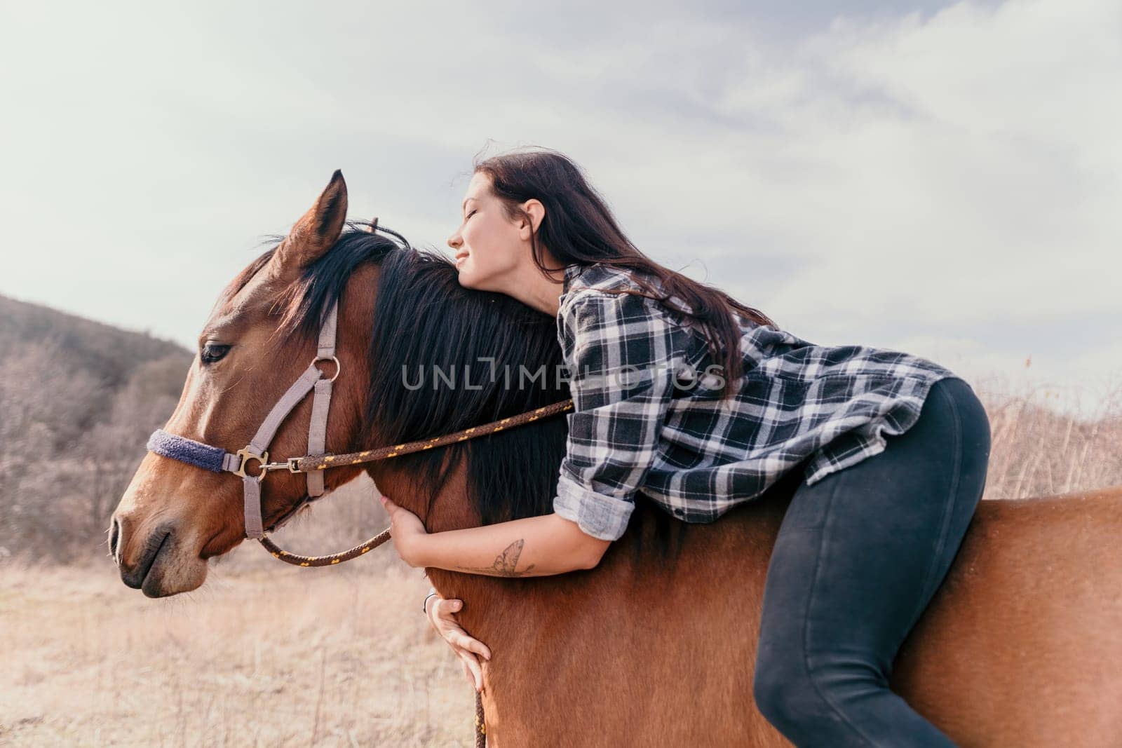 Cute happy young woman with horse. Rider female drives her horse in nature on evening sunset light background. Concept of outdoor riding, sports and recreation.