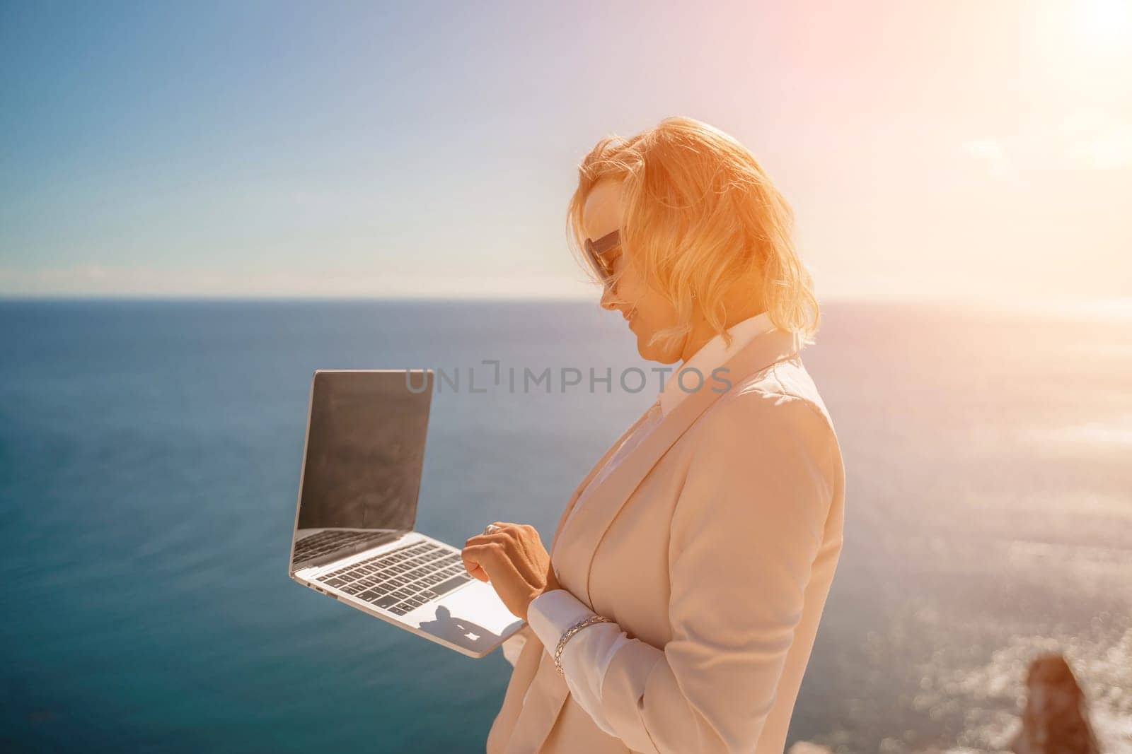 Freelance women sea working on the computer. Good looking middle aged woman typing on a laptop keyboard outdoors with a beautiful sea view. The concept of remote work. by Matiunina