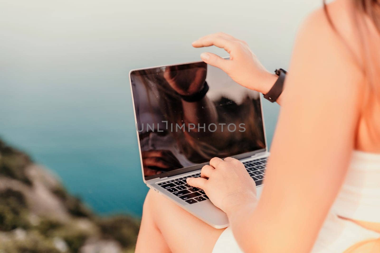 Freelance women sea working on the computer. Good looking middle aged woman typing on a laptop keyboard outdoors with a beautiful sea view. The concept of remote work. by Matiunina