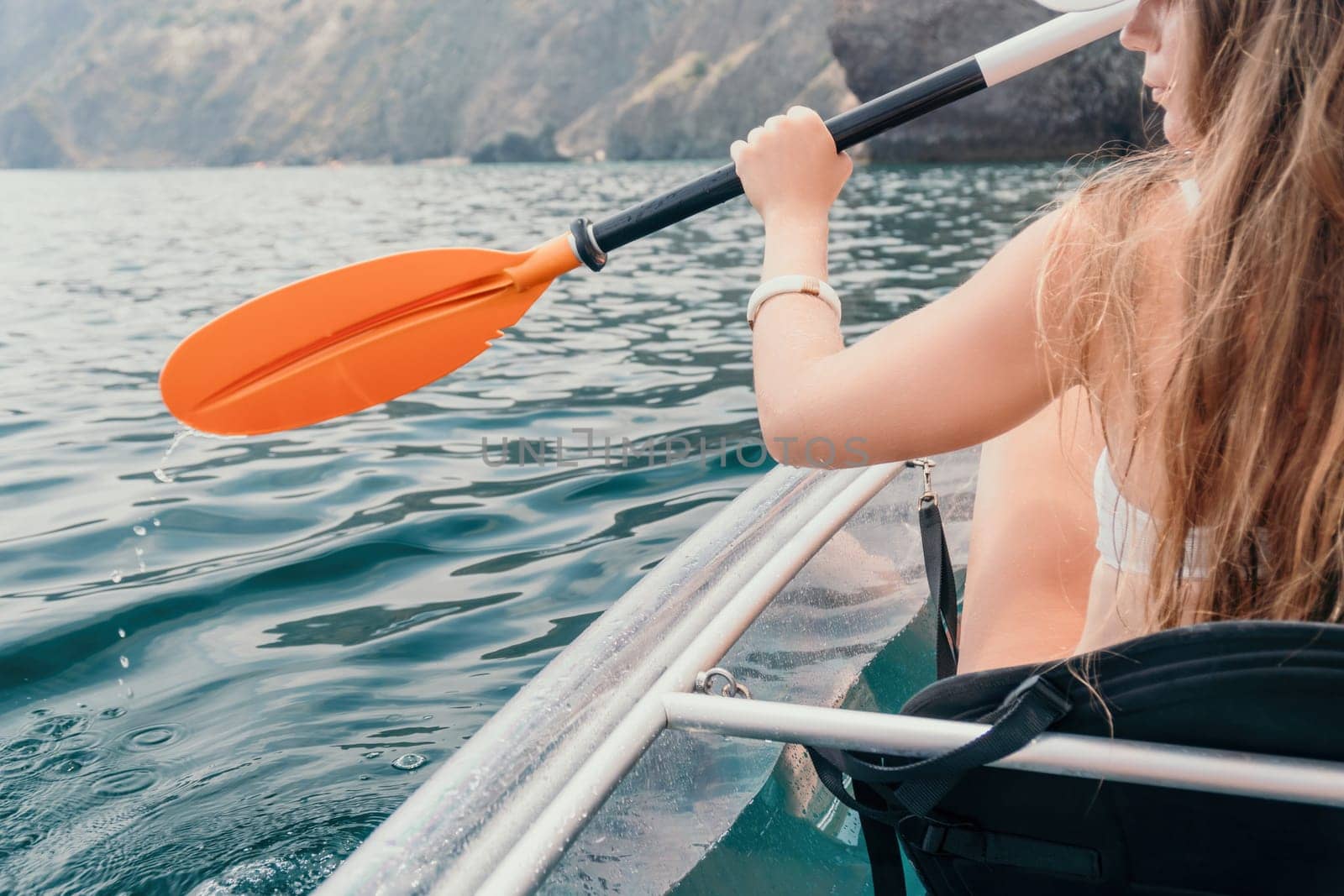 Woman in kayak back view. Happy young woman with long hair floating in transparent kayak on the crystal clear sea. Summer holiday vacation and cheerful female people having fun on the boat.