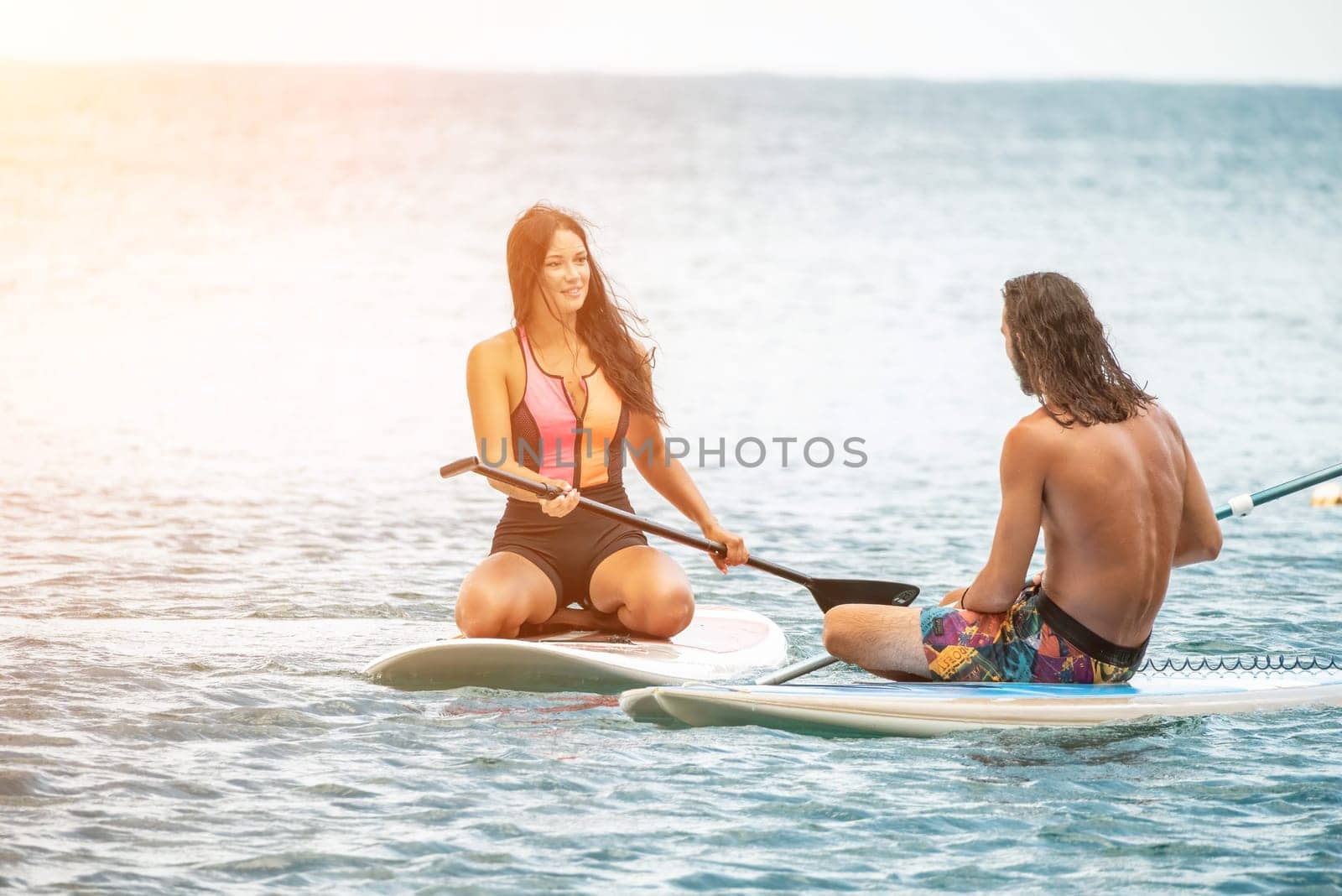 Sea woman and man on sup. Silhouette of happy young woman and man, surfing on SUP board, confident paddling through water surface. Idyllic sunset. Active lifestyle at sea or river