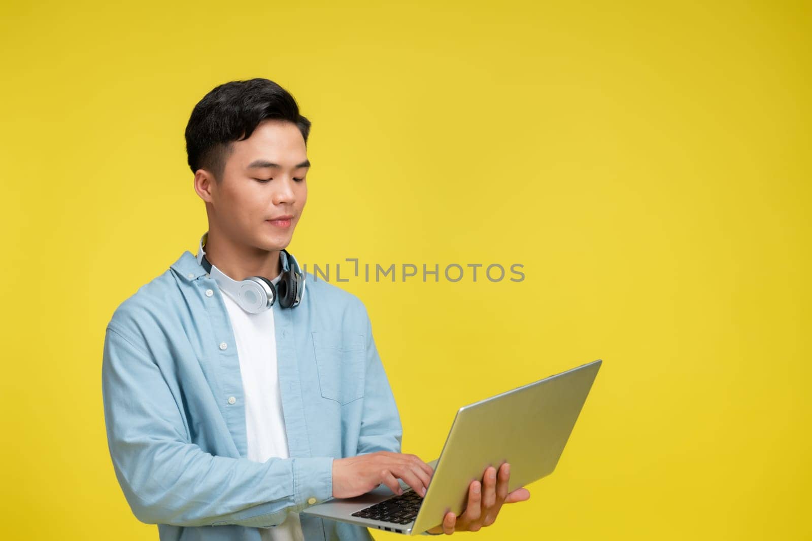 Smiling young man using laptop and looking at camera over yellow background