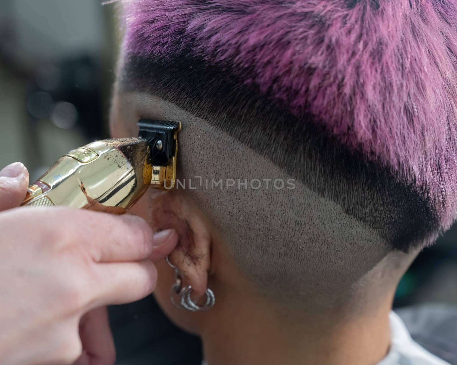 The hairdresser shaves the temple of a female client. Rear view of a woman with short pink hair in a barbershop