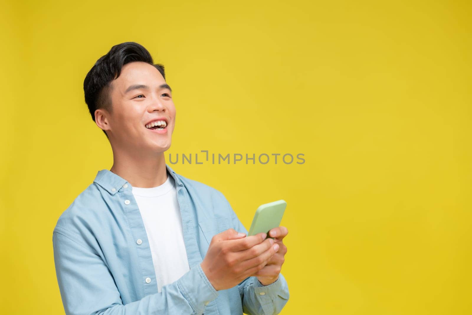 Shocked young Asian man looking at mobile phone screen reacting to online news with opened mouth