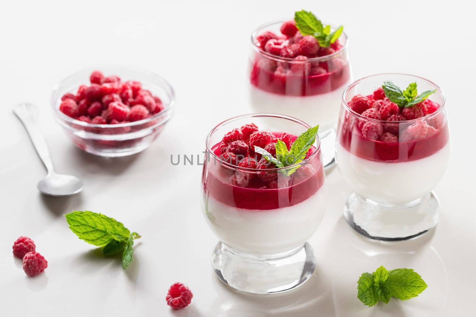 Panna cotta with raspberry jelly and mint leaves in glass glasses on a white table by galsand
