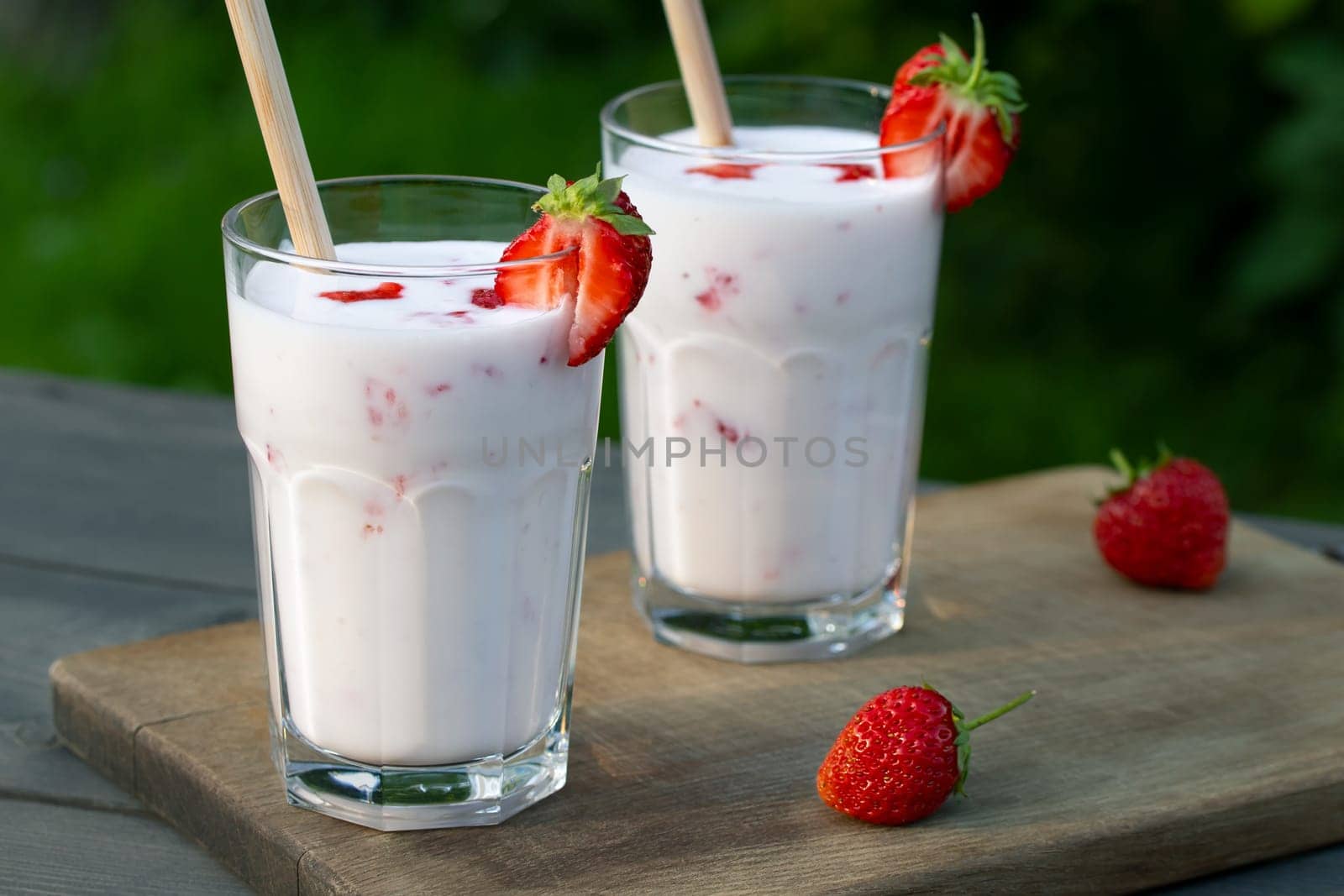 Strawberry smoothie in two glass glasses and fresh strawberries on a wooden table in the yard by galsand