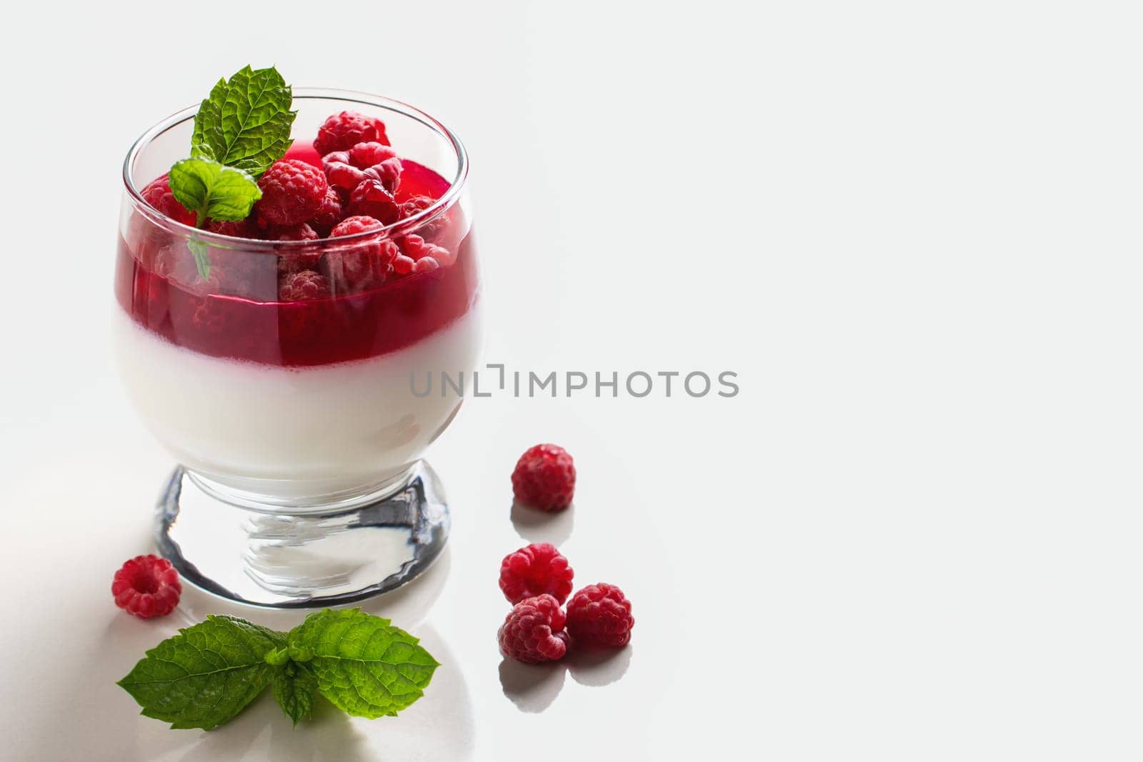Panna cotta with raspberry jelly and mint leaves in glass glasses on a white table, copyspace.