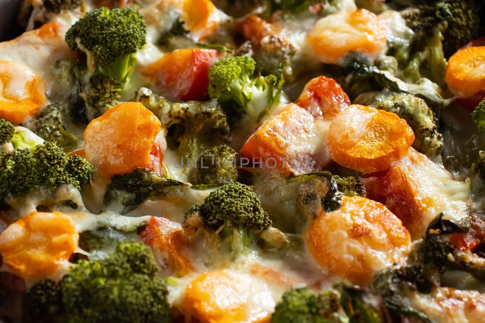 Gratin with broccoli, carrots and cheese baked in the oven on a dark wooden table, close up.