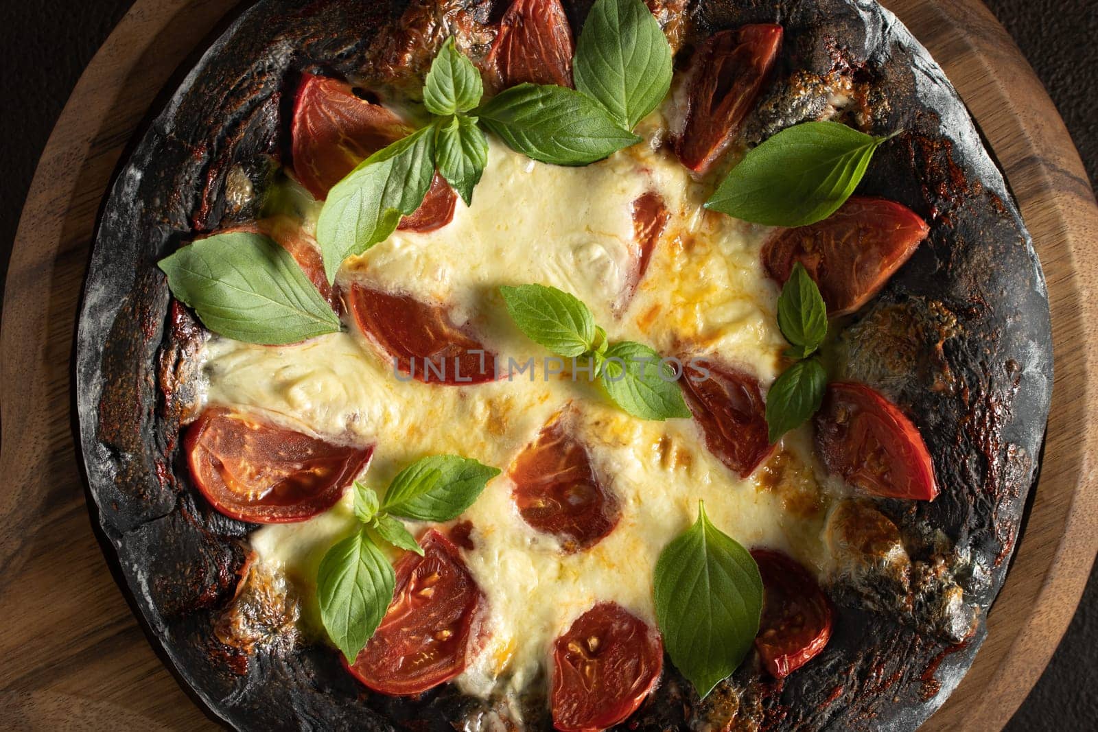 Black pizza margarita with tomatoes, mozzarella and basil. Dough with healthy bamboo charcoal powder, close up.