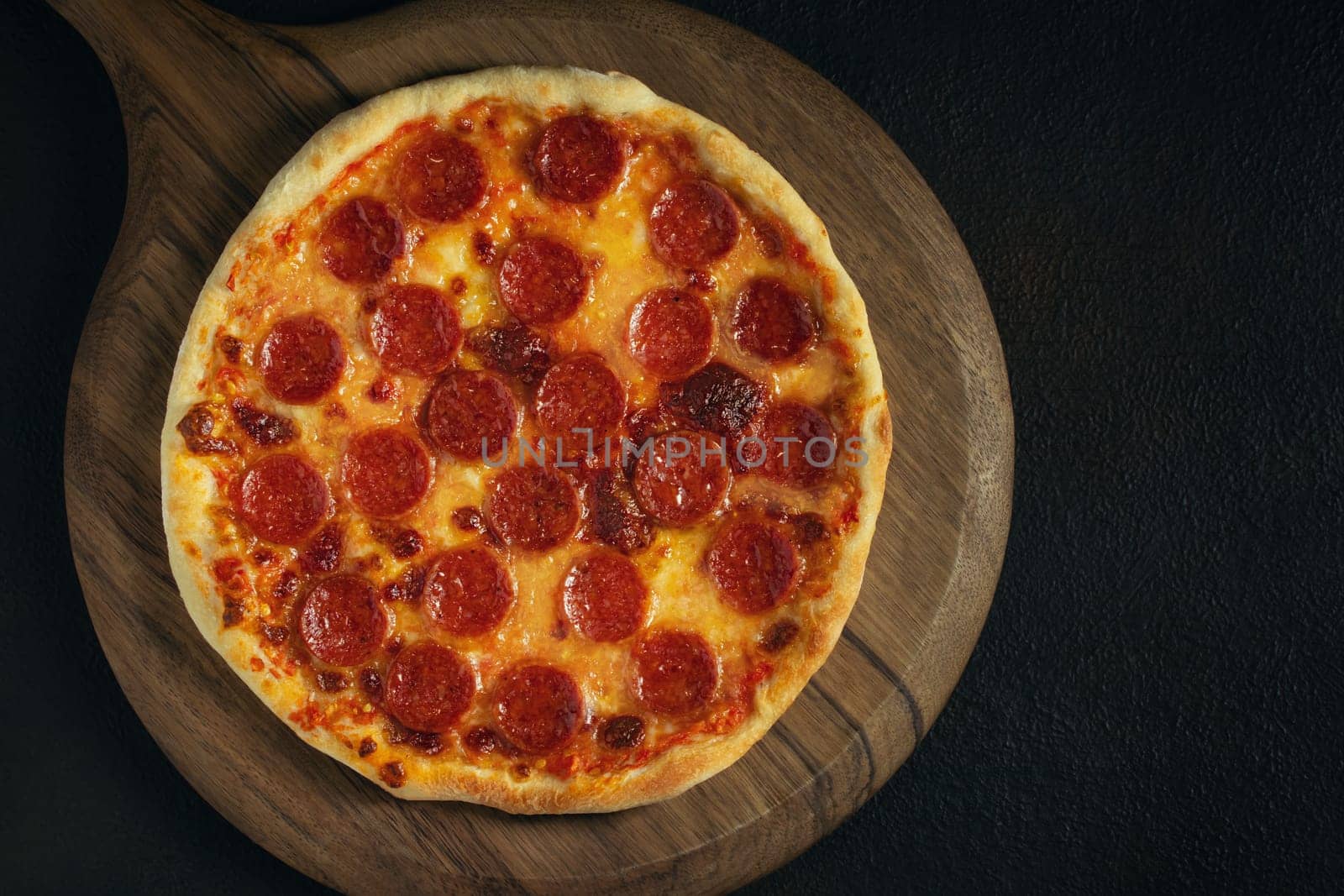 An uneven and slightly burnt homemade pepperoni pizza on a wooden tray on the table. Copyspace by galsand
