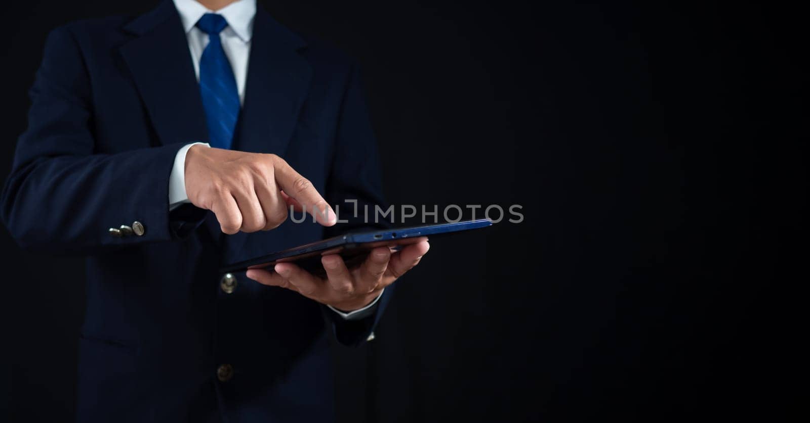 Businessman standing and holding tablet on dark background. Copy space. banner sign