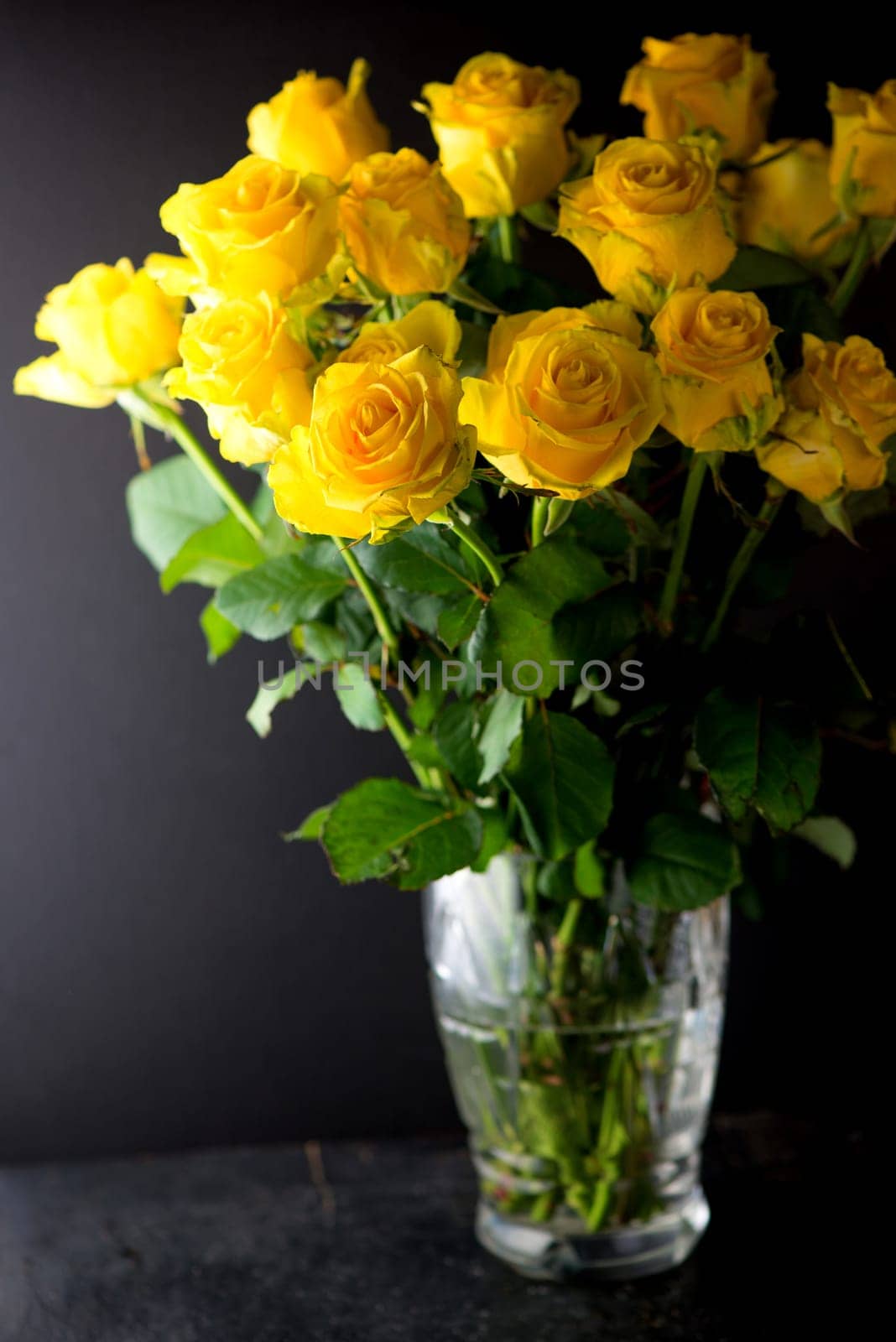 bouquet of beautiful yellow roses with leaves in a vintage crystal vase on a black background by aprilphoto