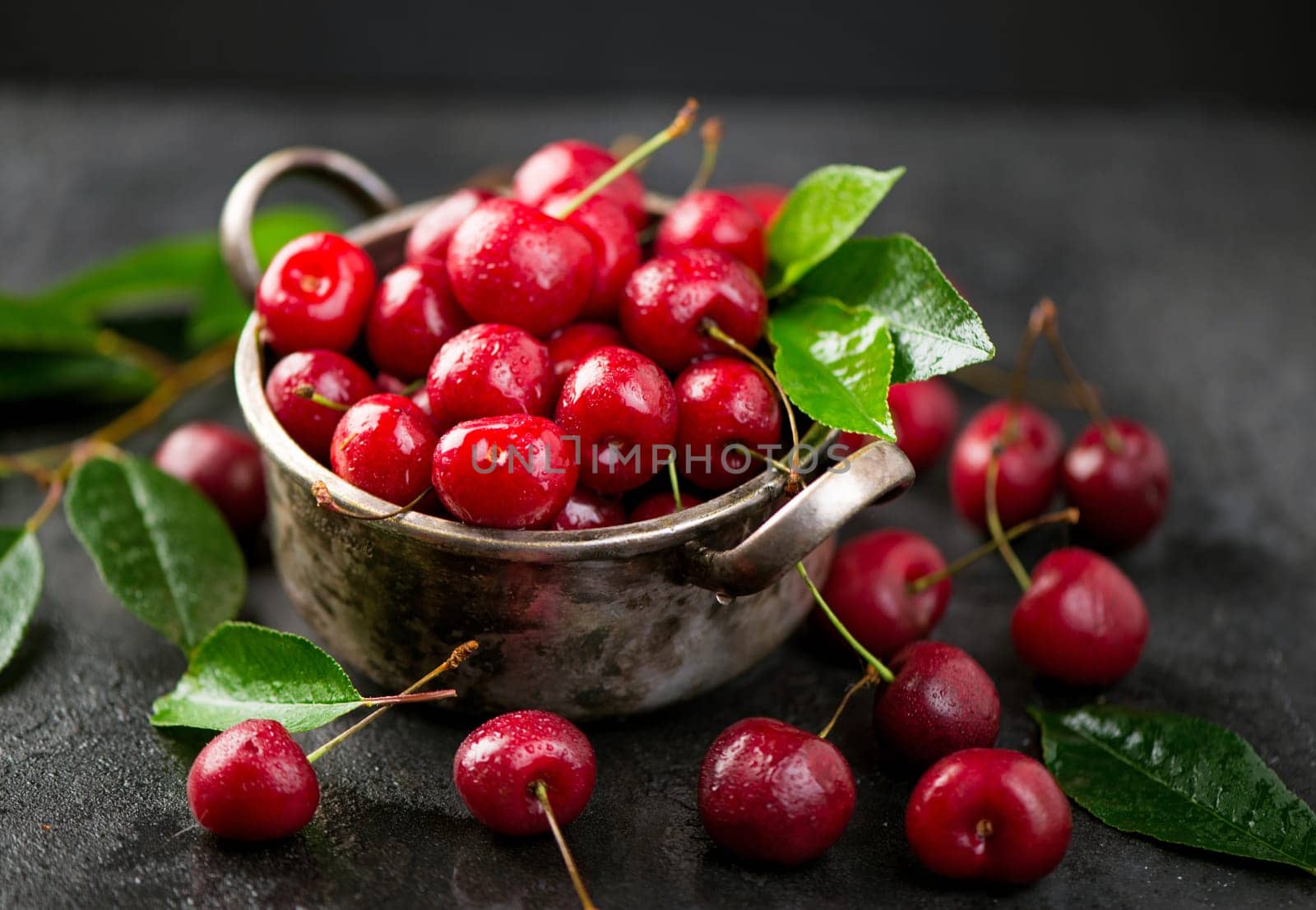 Seasonal harvesting of berries and fruits for the winter. Cherry jam. Cherry summer background. A large number of cherries with leaves on the table in a saucepan on a black background. close-up. by aprilphoto