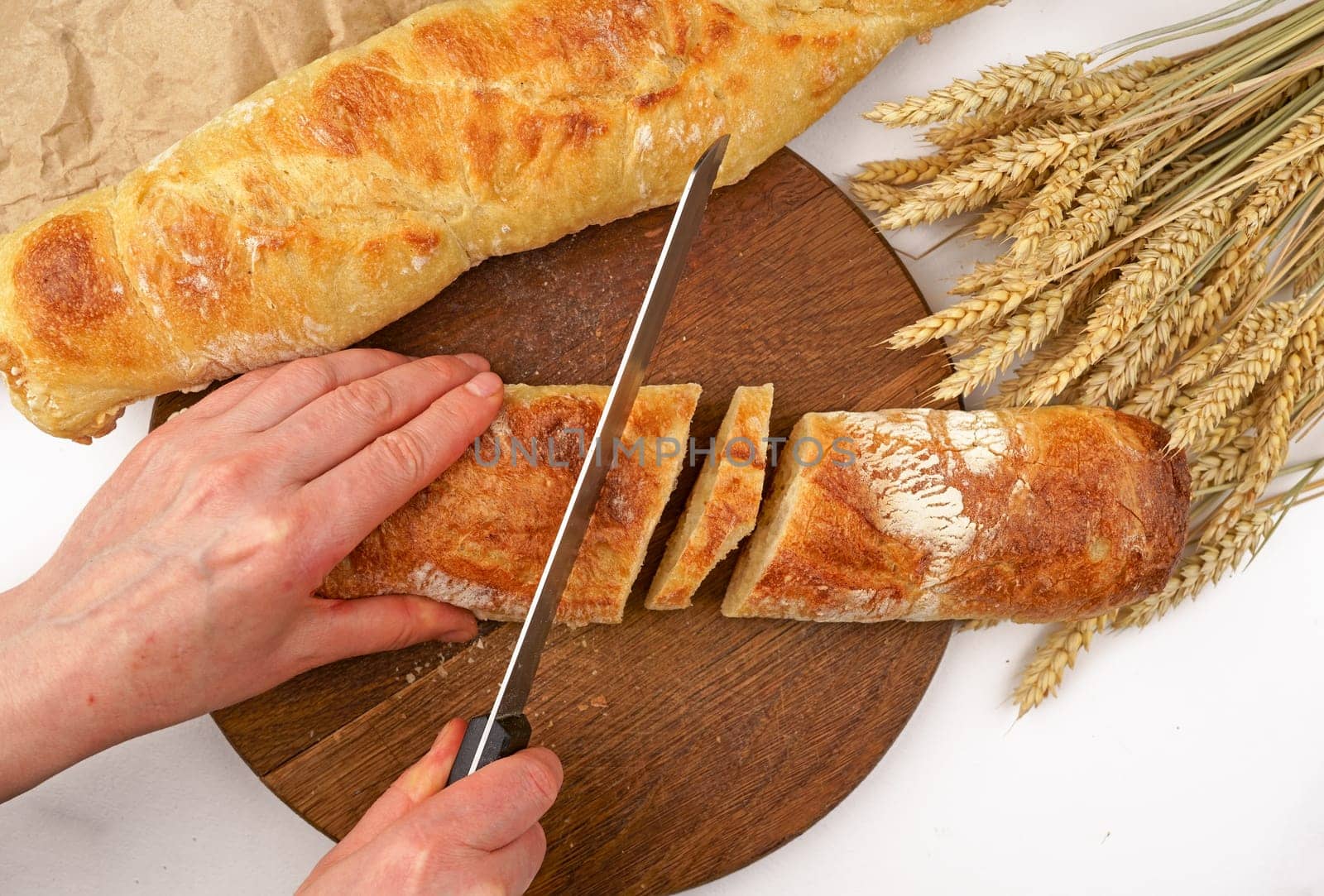 Slicing French Baguette On Slice For Bruschetta. Cutting Bread On Kitchen. Making Morning Breakfast. Fresh Bread On Table. Cutting French Baguette. Sliced White Wheat Baguette For Antipasto Bruschetta by aprilphoto