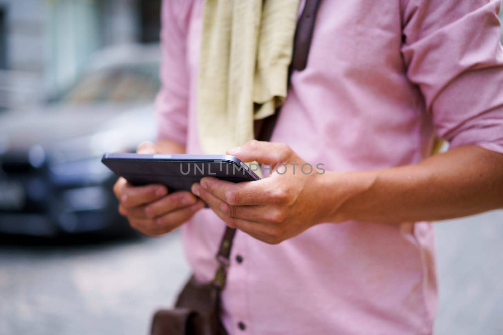 Close-up image, concept of digital communication comes to life as man's hands expertly hold tablet PC on bustling city street. Close-up perspective highlights details of touchscreen device, emphasizing its role in facilitating modern communication and information access. by LipikStockMedia