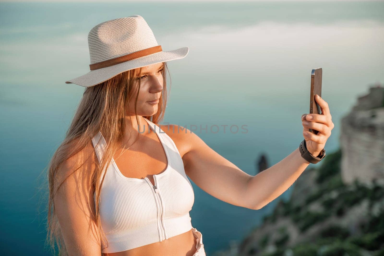 Selfie woman in hat, white tank top and shorts makes selfie shot mobile phone post photo social network outdoors on sea background beach people vacation lifestyle travel concept