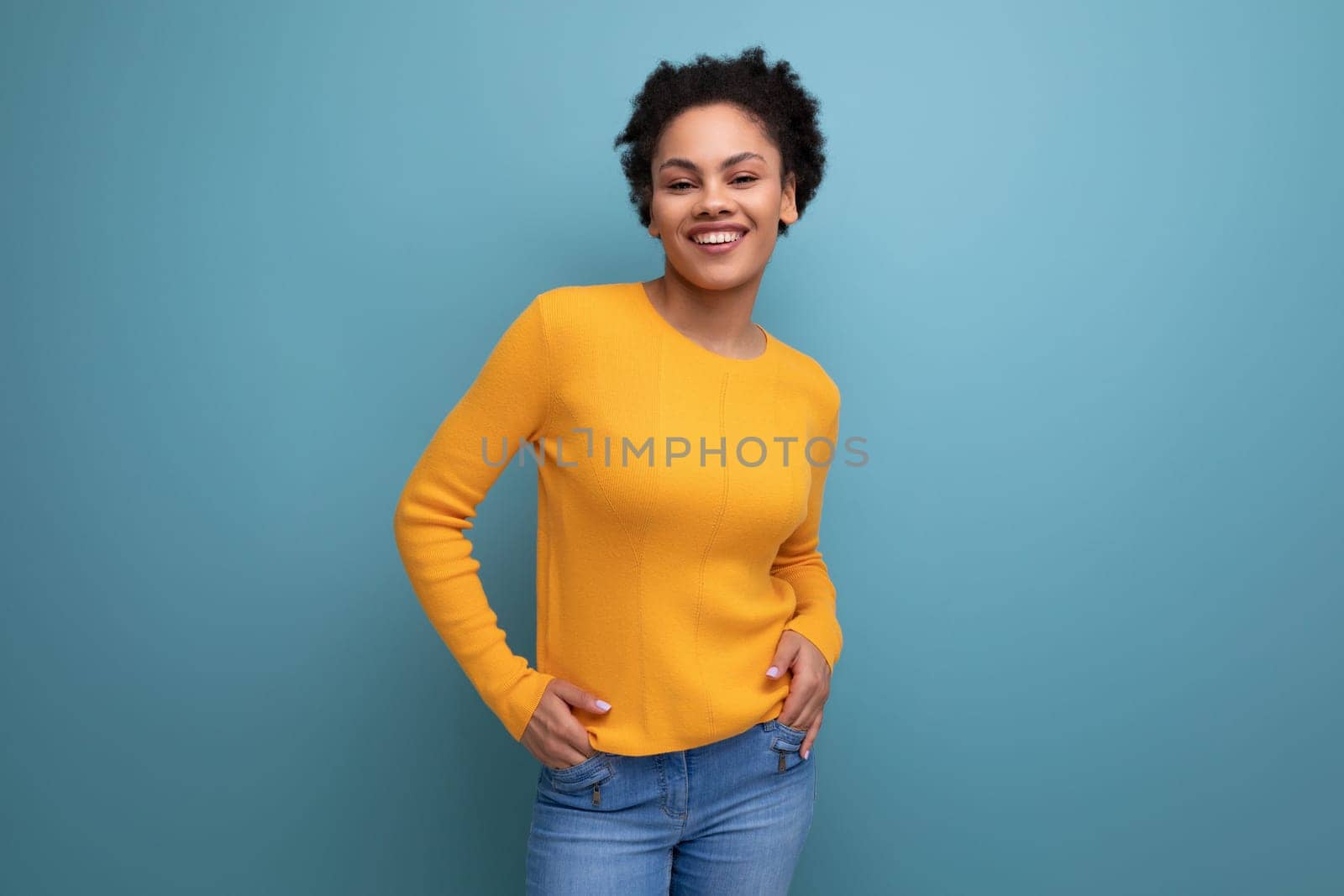 pretty confident 20s latin woman with afro hair in casual yellow sweater on studio background with copy space.