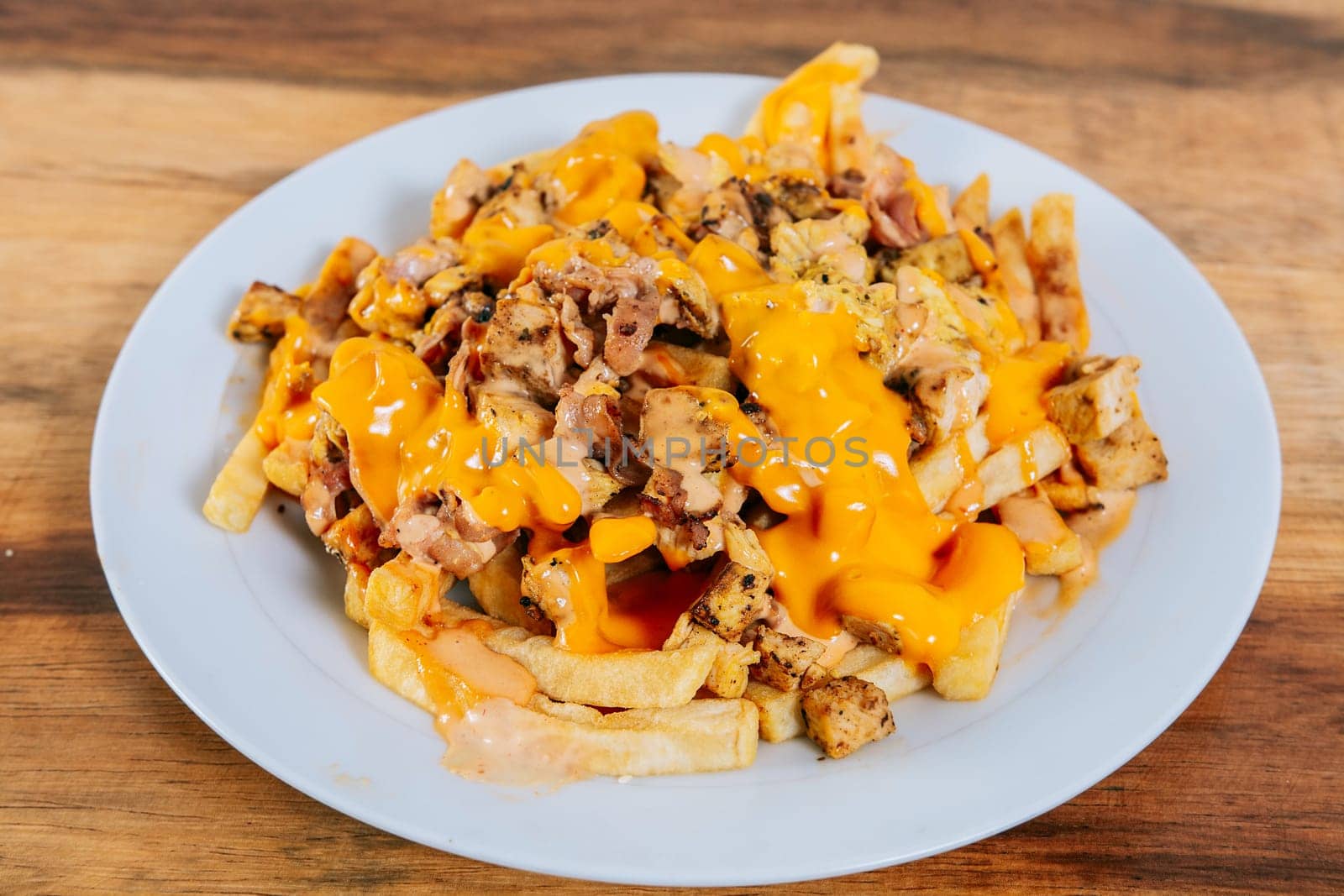 Plate of chicken nachos with potatoes and melted cheese on table. Traditional chicken nachos with melted cheese by isaiphoto