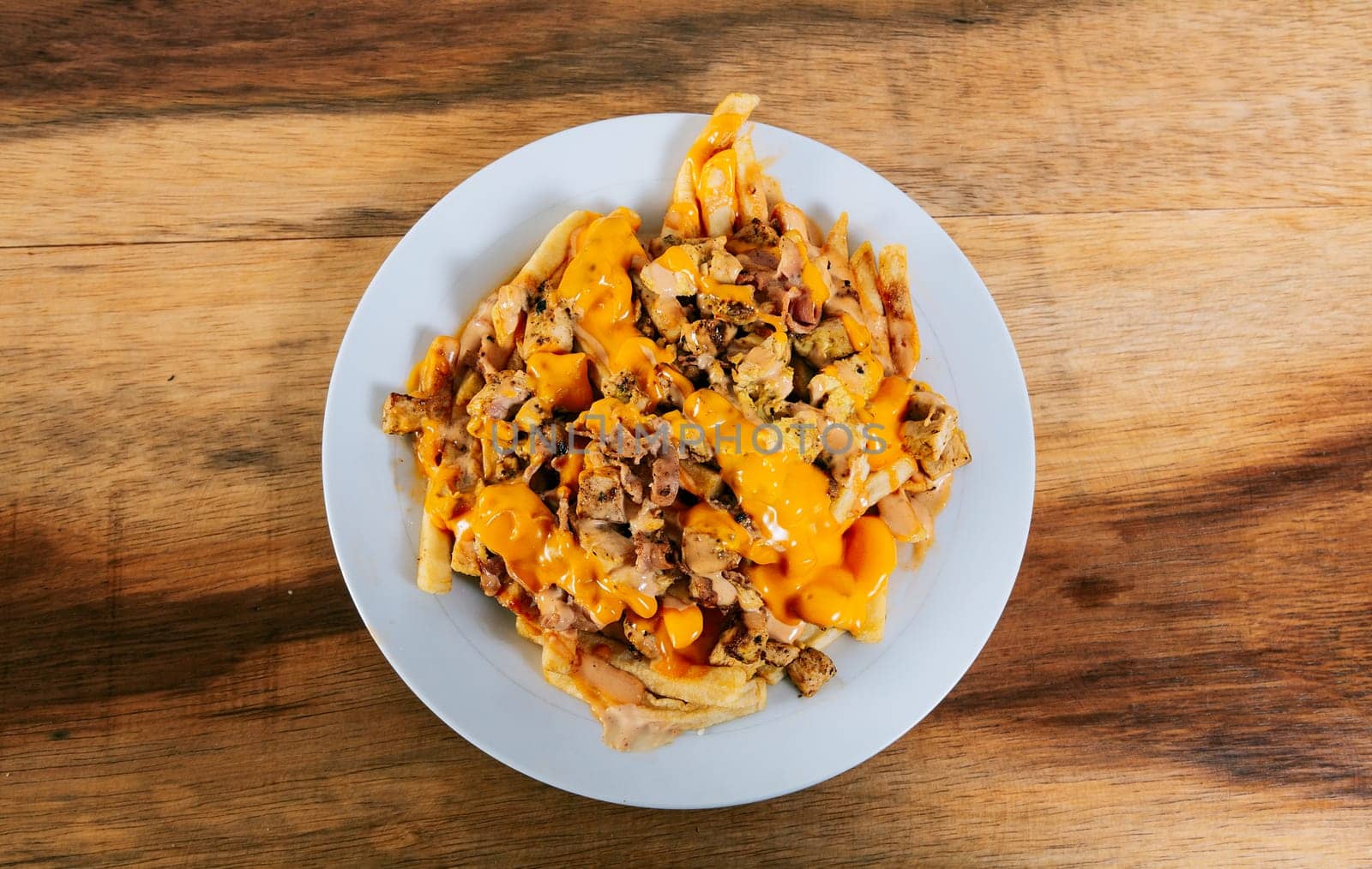 Top view of chicken nachos with melted cheese. Plate of chicken nachos with melted cheese on wooden table by isaiphoto