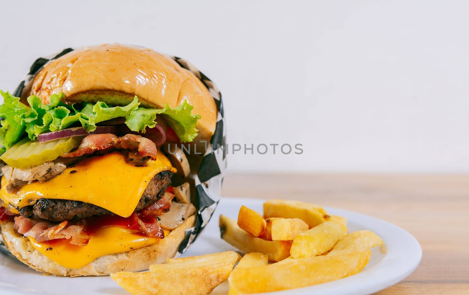 Homemade burger with french fries on a plate on wooden table. Big cheeseburger with fries served with copy space